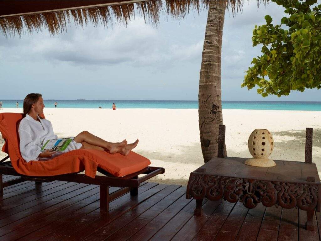 woman laying on orange lounge chair under shade on white sand beach