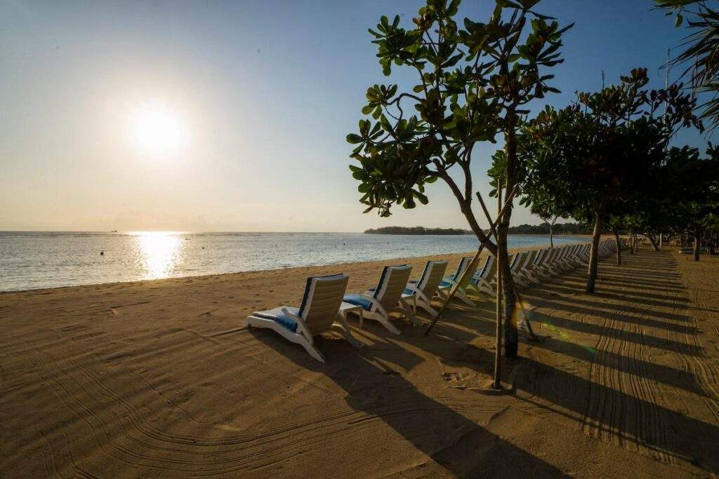 lawn chairs on the beach with sun over the water