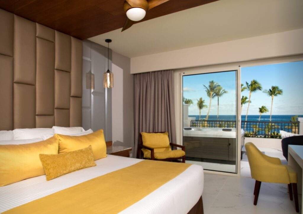 white bed with gold pillows with sliding door overlooking beach
