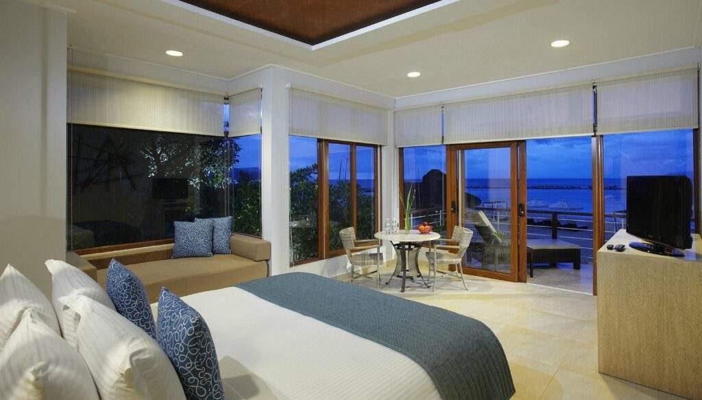 white bed with wall to wall floor to ceiling windows overlooking ocean at night