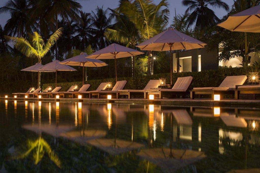 lighted tropical pool at night with 5 umbrellas and chairs