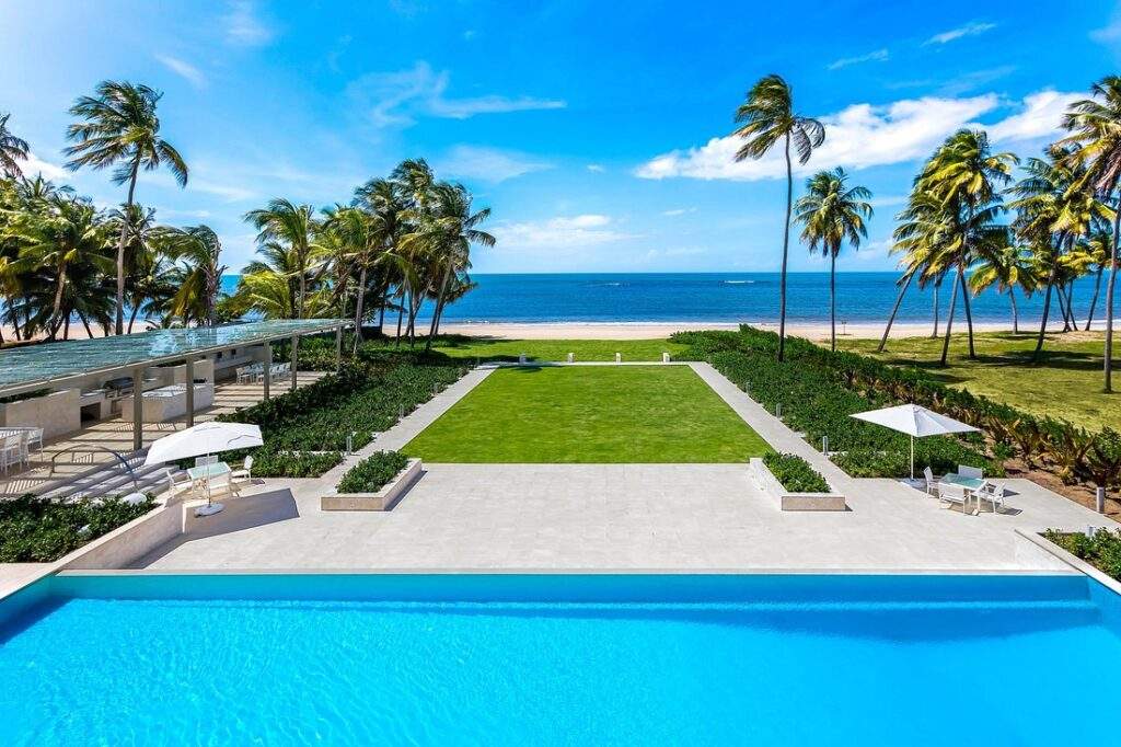 square resort swimming pool in front of grassy field in front of beach