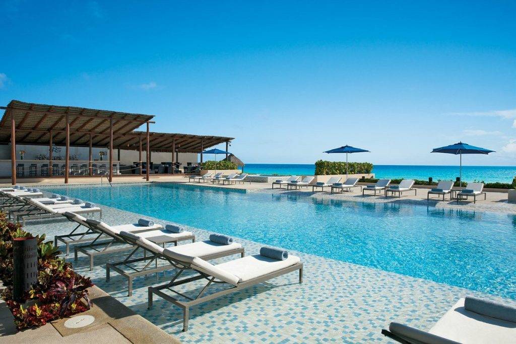 lounge chairs next to rectangular resort pool with ocean in background
