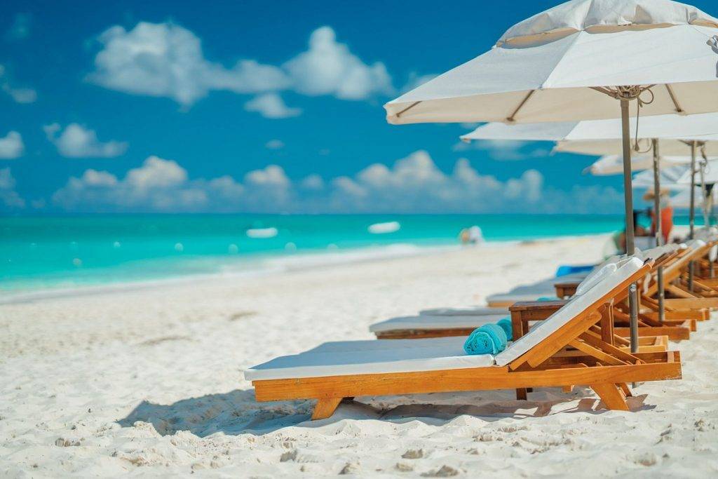 row of lounge chairs under umbrellas on white sand beach