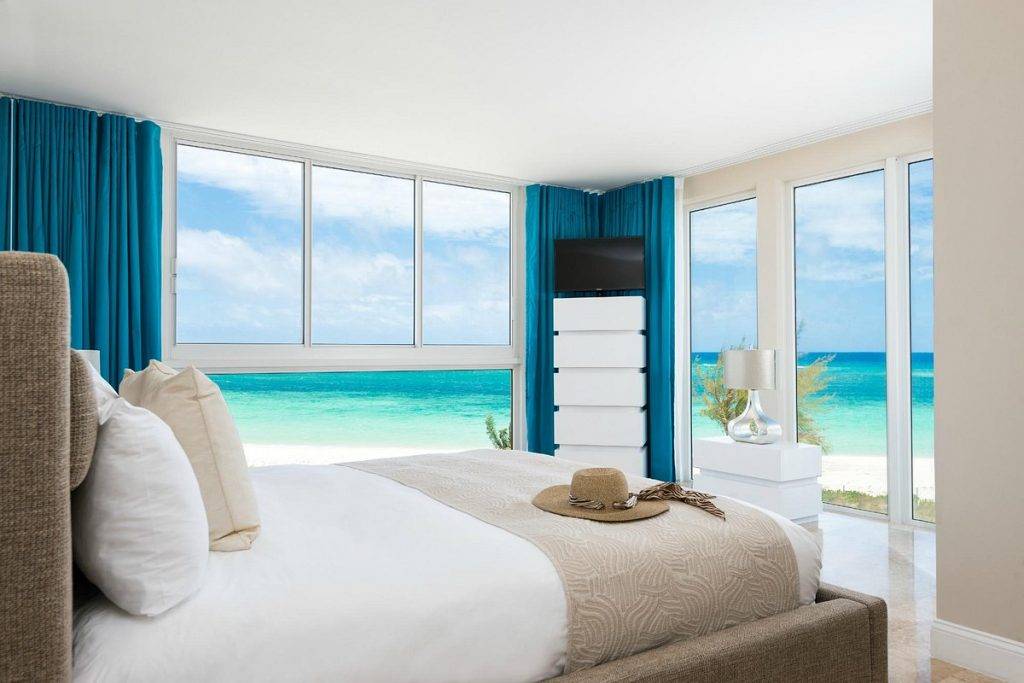 bed in resort room with floor to ceiling windows on all walls looking out to ocean