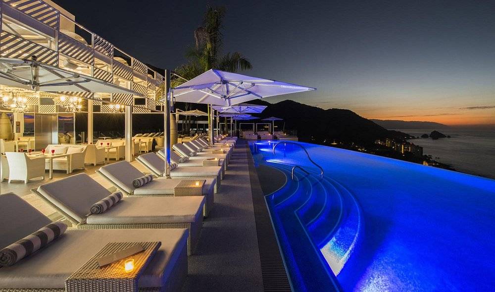 blue lighted pool at night lined with lounge chairs and umbrellas