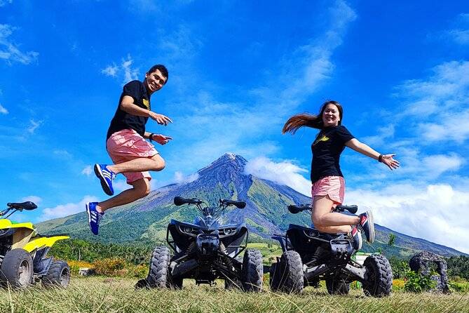 couple jumping in front of ATVs and mountain