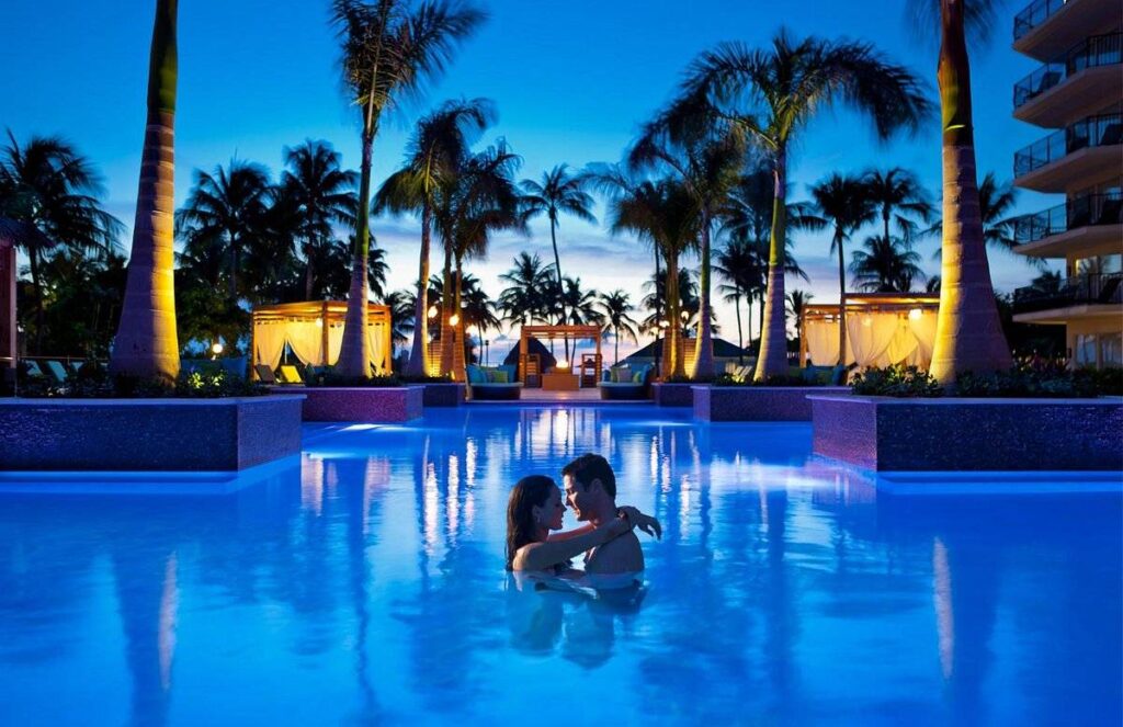 couple in blue lighted pool at sunset