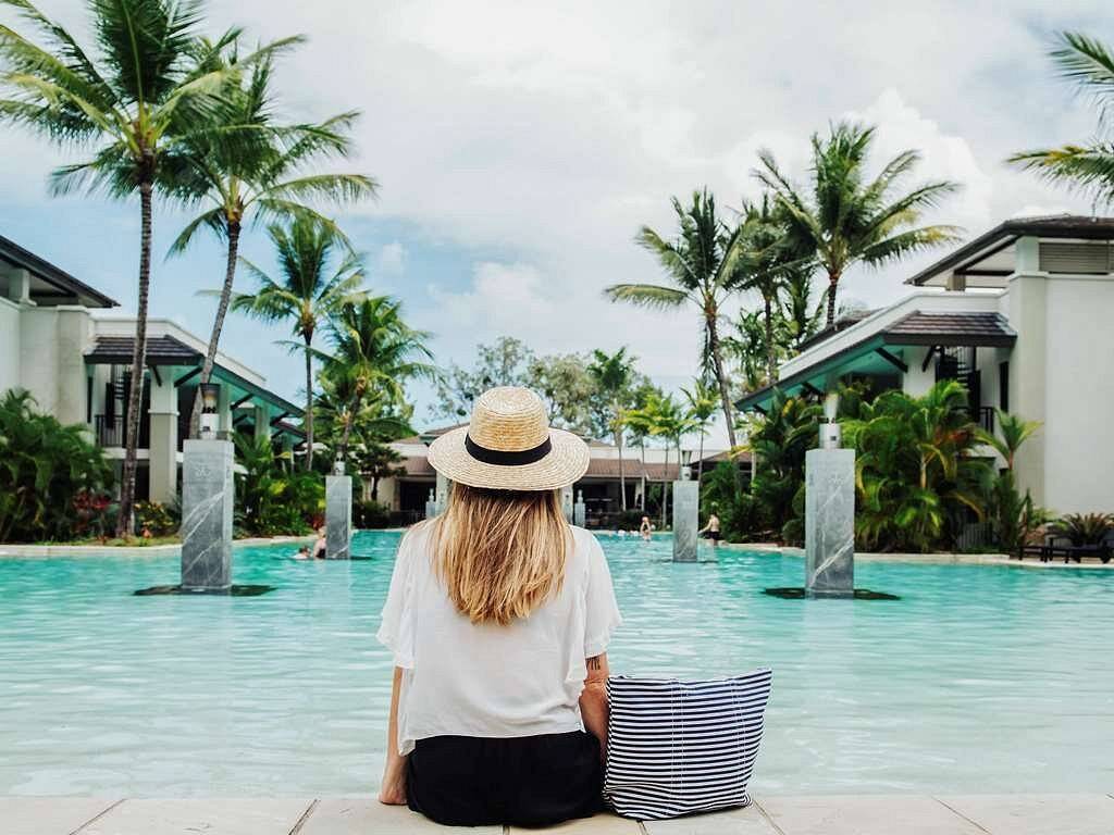 woman in hat sitting at resort pool with palm trees
