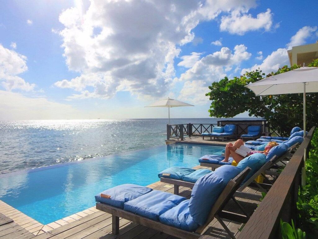 woman sitting on one of 7 blue lounge chairs in front of infinity pool at ocean