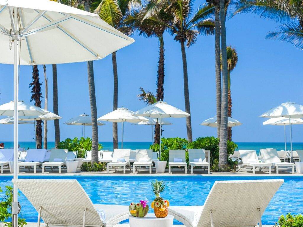 white lounge chairs and white umbrellas around pool at beach