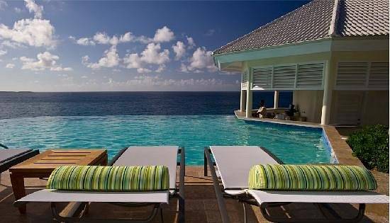 two lounge chairs with green pillows next to infinity pool