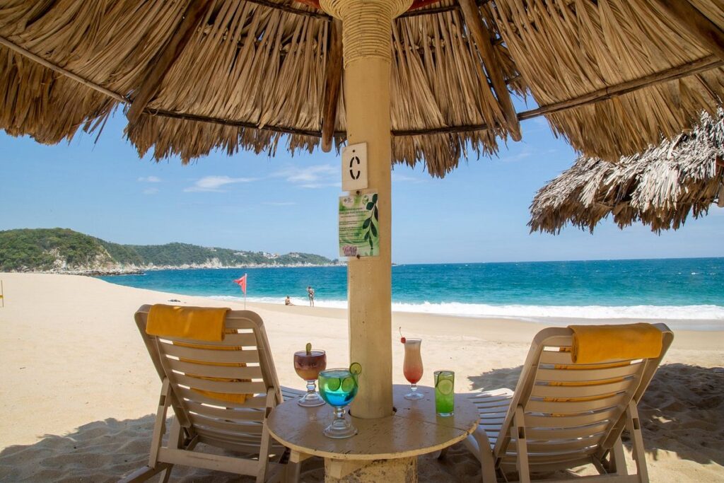 two lounge chairs under grass umbrella on beach